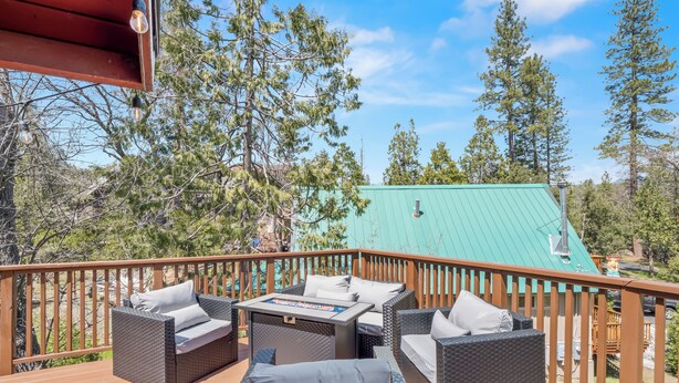 A deck with wicker furniture and a view of a house with a green roof. - New! Arcade Games, Hot Tub,  Fire Pit, BBQ, 3:2 (Oakhurst)