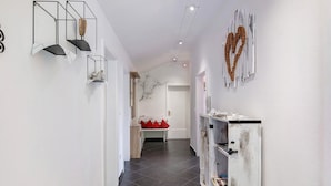 Un couloir avec un mur blanc, un banc en bois avec des coussins rouges et une armoire blanche avec des étagères.