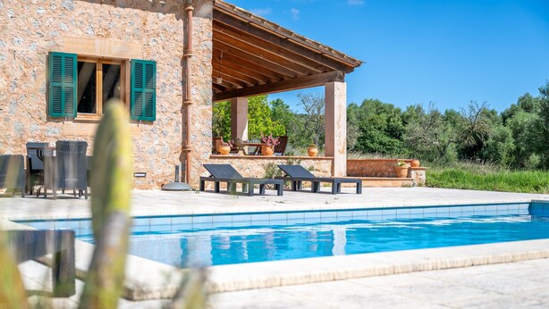 Ein Steinhaus mit Pool, Sitzmöglichkeiten im Freien und einer Pergola.