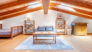 Ein gemütliches Dachzimmer mit Holzbalkendecke, einem Sofa, einem Tisch mit Untersetzern und einem Schrank.