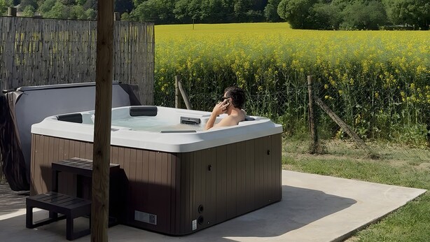 Un jacuzzi con un pérgola de madera, una mesa y una silla, con vistas a un campo y una colina.