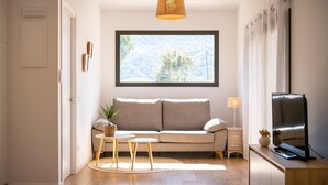 Una sala de estar moderna con un sofá, una mesita, un televisor y una ventana con vistas a árboles.