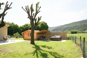 A wooden cabin with a hot tub, a covered seating area, and a fenced yard.