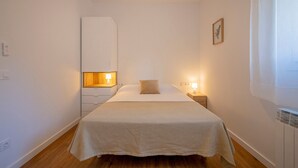 Un dormitorio con cama, lámparas de noche, mesita de noche, armario y un cuadro en la pared.