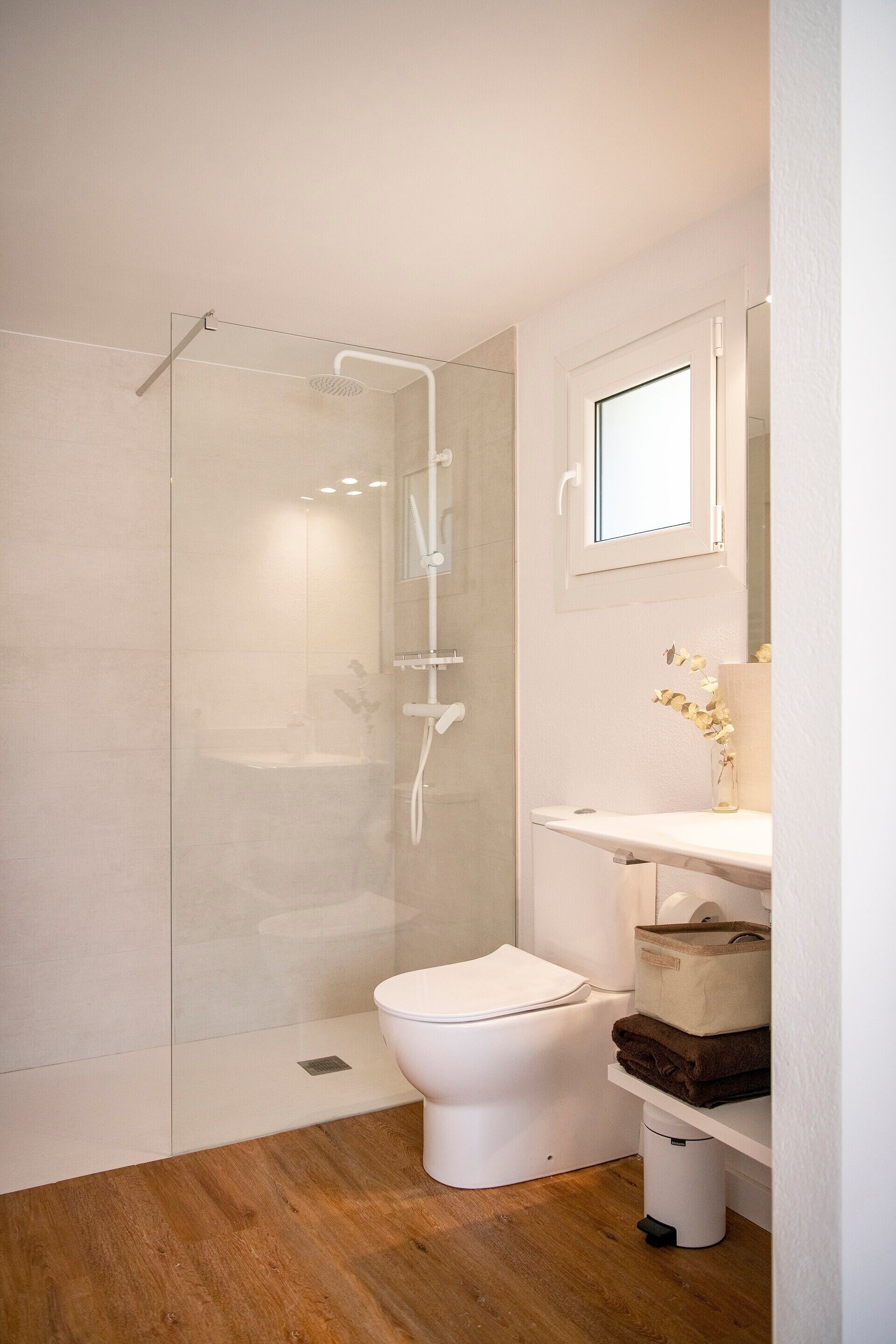 A modern bathroom with a glass-enclosed shower, a white toilet, and a wooden floor.