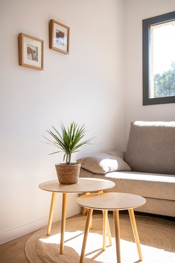 Una habitación con una mesa redonda de madera, una planta en maceta, un sofá y dos cuadros en la pared.