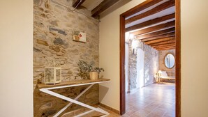 A stone wall, wooden beams, a tiled floor, a white shelf with decorative items, and a doorway leading to another room. - Holiday Home 'L'Altell' with Mountain Views, Wi-Fi and Air Conditioning (Montagut)