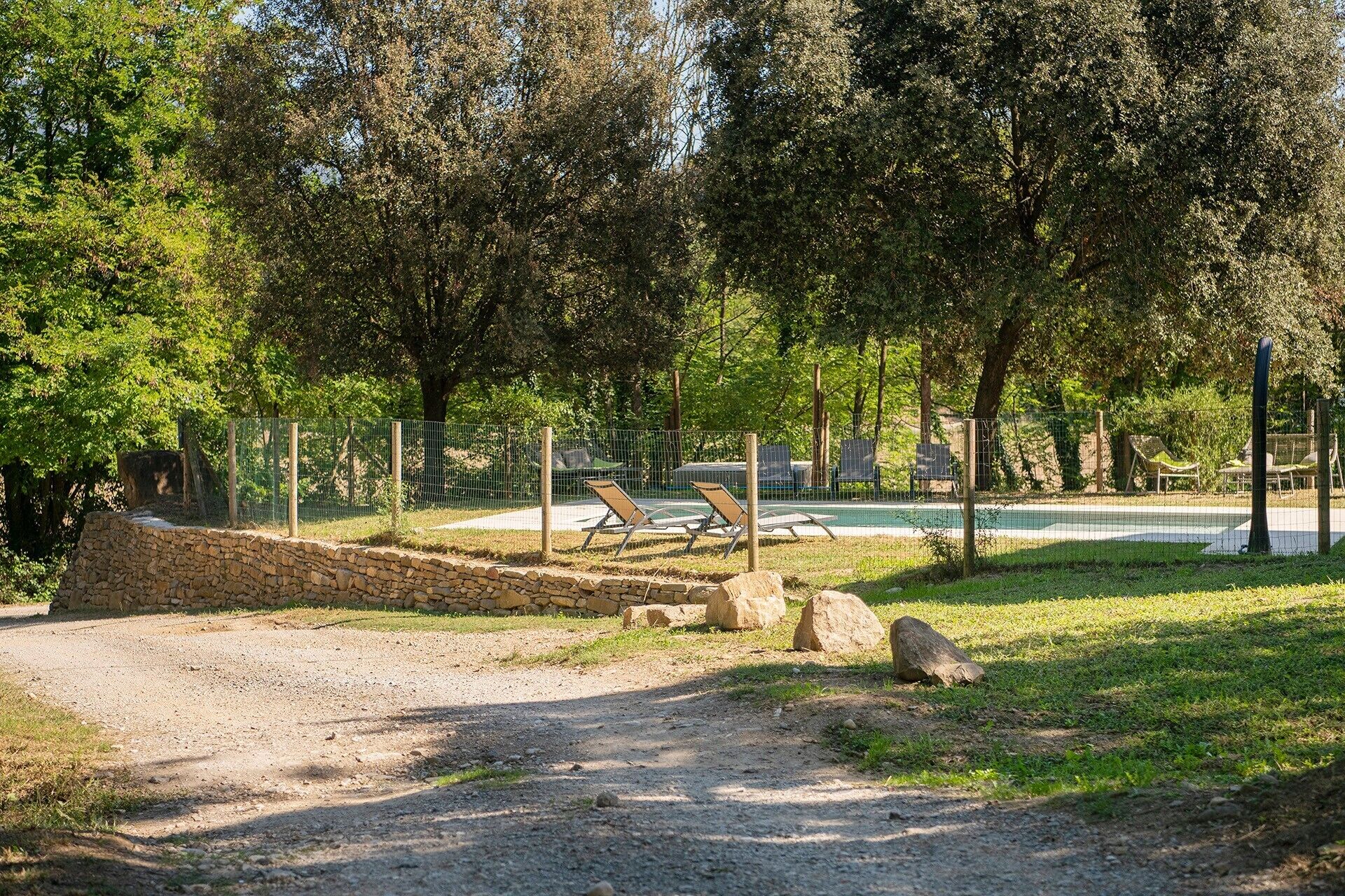Un'area esterna recintata con un sentiero sterrato, poltrone da relax e una piscina.