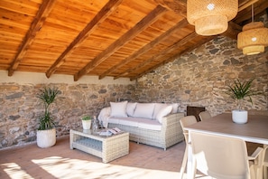 Una habitación acogedora con pared de piedra, vigas de madera en el techo, muebles de mimbre e iluminación colgante.