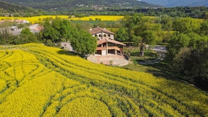 Une maison de campagne avec un toit en pierre, entourée de champs de fleurs jaunes, et offrant une vue dégagée sur la campagne.