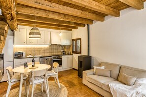 A kitchen with wooden beams, white cabinets, a dining table with chairs, and a sofa in a living area.