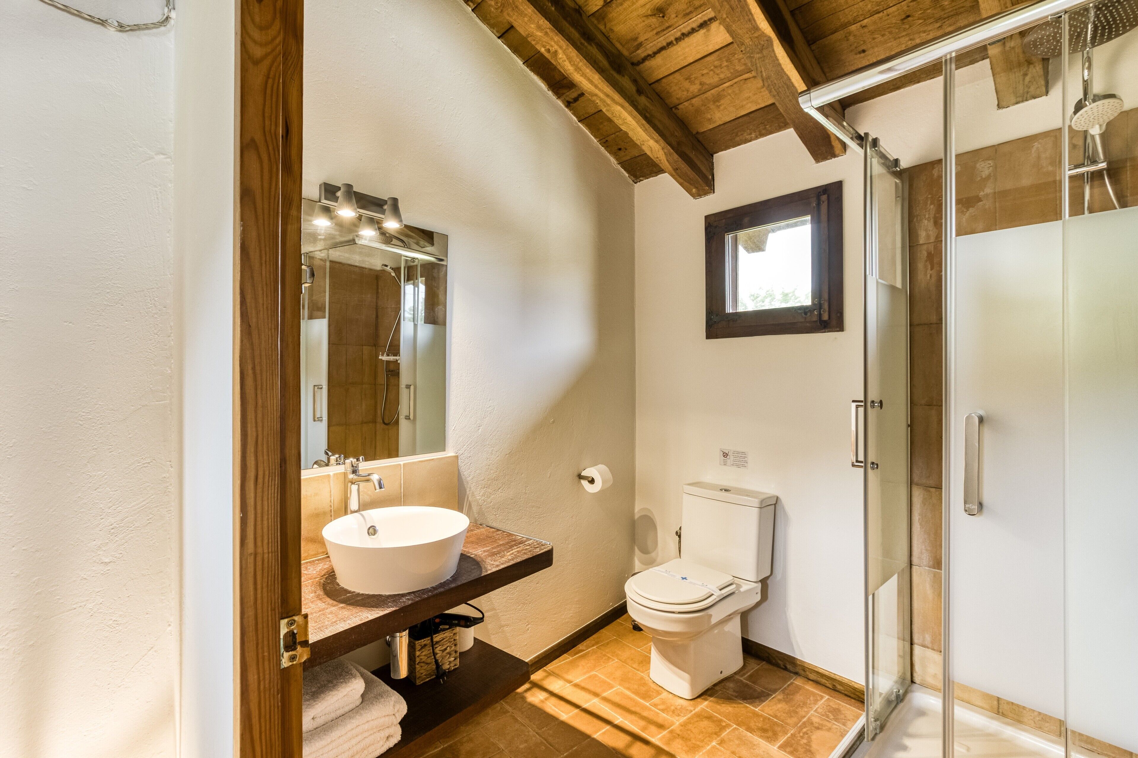 A bathroom with a wooden ceiling, a glass shower enclosure, a white sink, and a toilet.