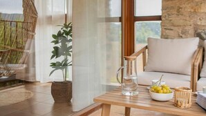 Une pièce chaleureuse avec un mur en pierre, un plafond en bois, une chaise en osier, une table avec un pichet et un bol, et une plante en pot.