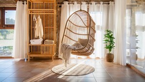 Une pièce avec un fauteuil suspendu, une armoire en bois contenant des serviettes, une plante en pot et une vue par la fenêtre.