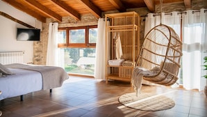 Une chambre à coucher comprenant un lit, un fauteuil suspendu, une armoire en bois et un téléviseur.