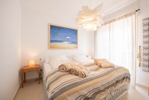 A bedroom with a bed, a painting of a beach, a bedside lamp, and a window with curtains.