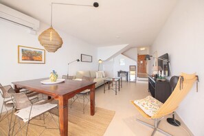 A modern living room with a wooden dining table, a sofa, a chair, and a hanging light fixture.
