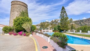 A stone tower, a swimming pool, and a paved walkway with greenery. - Apartment 'Casa Emma' with Sea Views, Wi-Fi and Air Conditioning (Almuñécar)