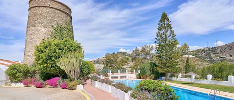 Una torre de piedra, una piscina y un camino pavimentado con vegetación.