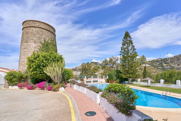 A stone tower, a swimming pool, and a paved walkway with greenery.