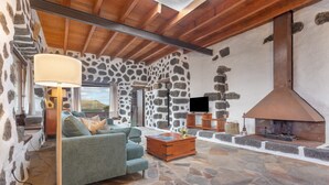 A stone-walled room with a fireplace, a sofa, a lamp, and a television.
