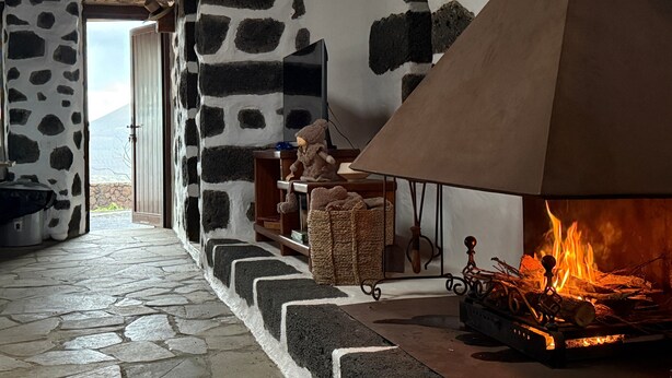 A stone-walled interior with a fireplace, a stone floor, and a view through an open door.