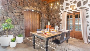A stone-walled dining area with a wooden table, chairs, and potted plants.