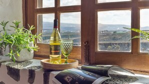 A window with a view of a landscape, a bottle of wine, a glass, and a potted plant on a windowsill.