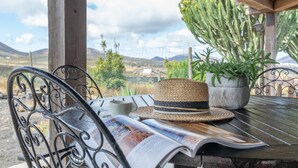 A wooden pergola with a table, a hat, a potted plant, and a magazine.