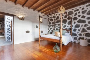 A four-poster bed with a wooden frame and a straw hat on top, a stone wall, and a wooden ceiling. - 'El Rincón de Guatisea' with Mountain Views, Private Terrace & Wi-Fi (San Bartolomé)