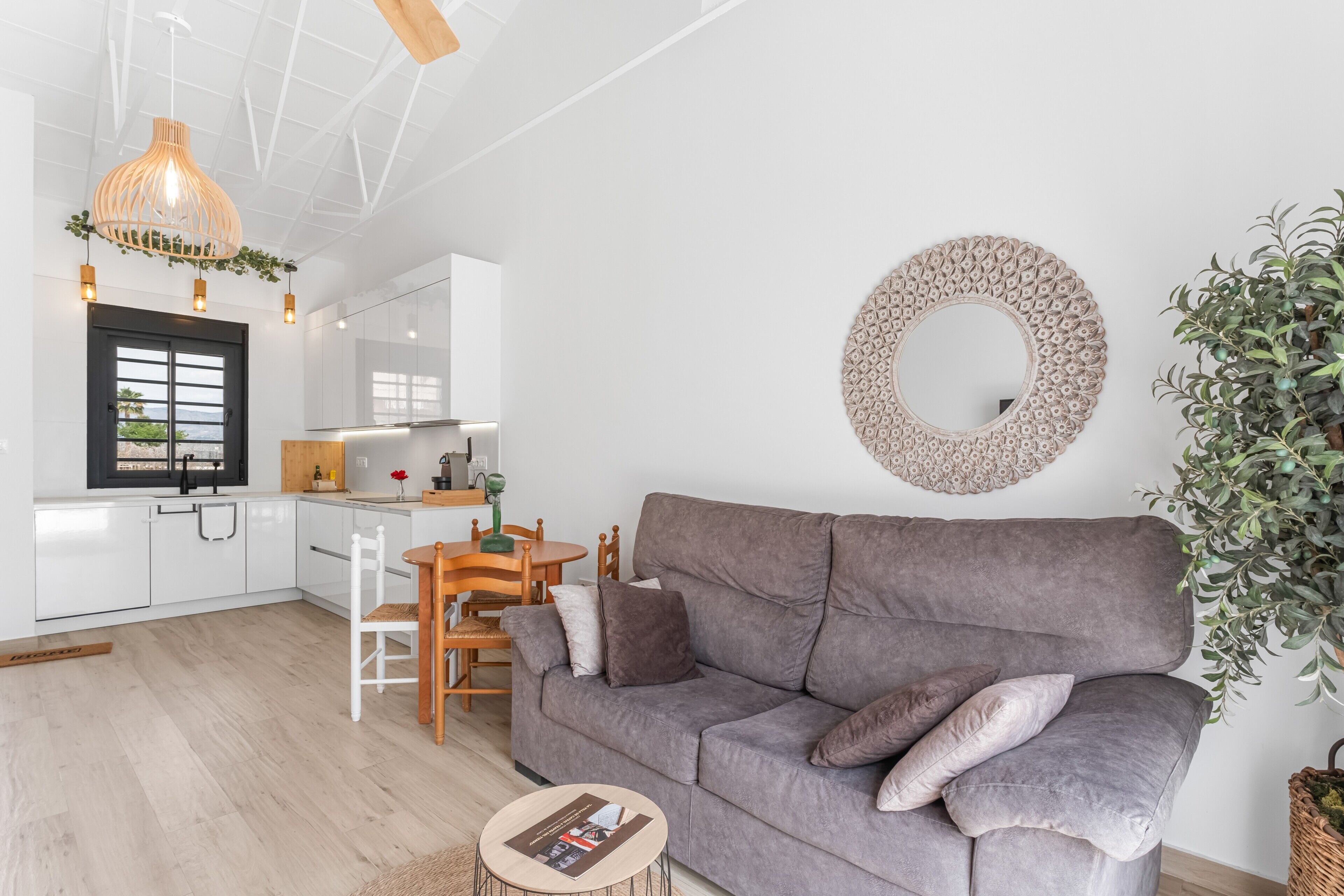Ett modernt vardagsrum med en grå soffa, en rund spegel och en matplats med ett träbord och stolar.