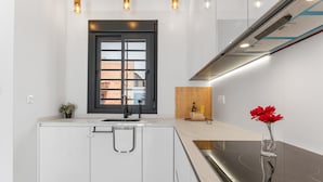 Una cucina moderna con mobili bianchi, una finestra con cornice nera, piano cottura integrato e illuminazione a sospensione.