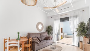 Un soggiorno moderno con divano, tavolo da pranzo, sedie, ventilatore a soffitto, un grande specchio e vista sull'esterno.