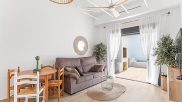 A modern living room with a sofa, dining table, chairs, a ceiling fan, a large mirror, and a view to the outside.
