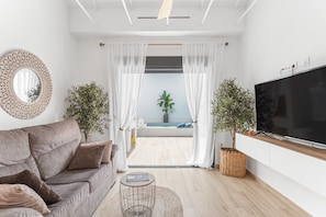 Un soggiorno moderno con un divano, una televisione, un tavolino e vista su un balcone con una pianta e una finestra.