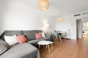 Una sala moderna con un sofá gris, una mesita blanca y un comedor con una silla verde.