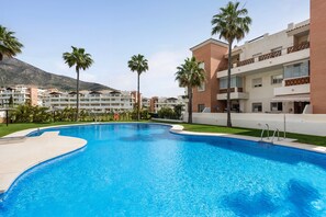 Una piscina con agua cristalina azul, rodeada de palmeras y un edificio con balcones.