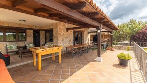 Une terrasse extérieure avec une table de baby-foot, des murs en pierre, des poutres en bois et une rambarde.