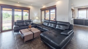 Un salon moderne avec un canapé d’angle, une table basse et de grandes fenêtres donnant sur l’extérieur.