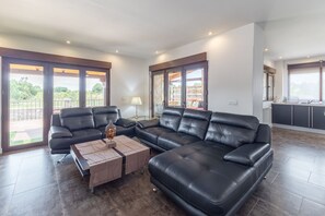 Een moderne woonkamer met een hoekbank, een salontafel en grote ramen met uitzicht op de omgeving.