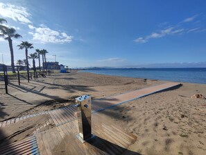 Ein Strand mit Holzsteg, Palmen und blauem Himmel.