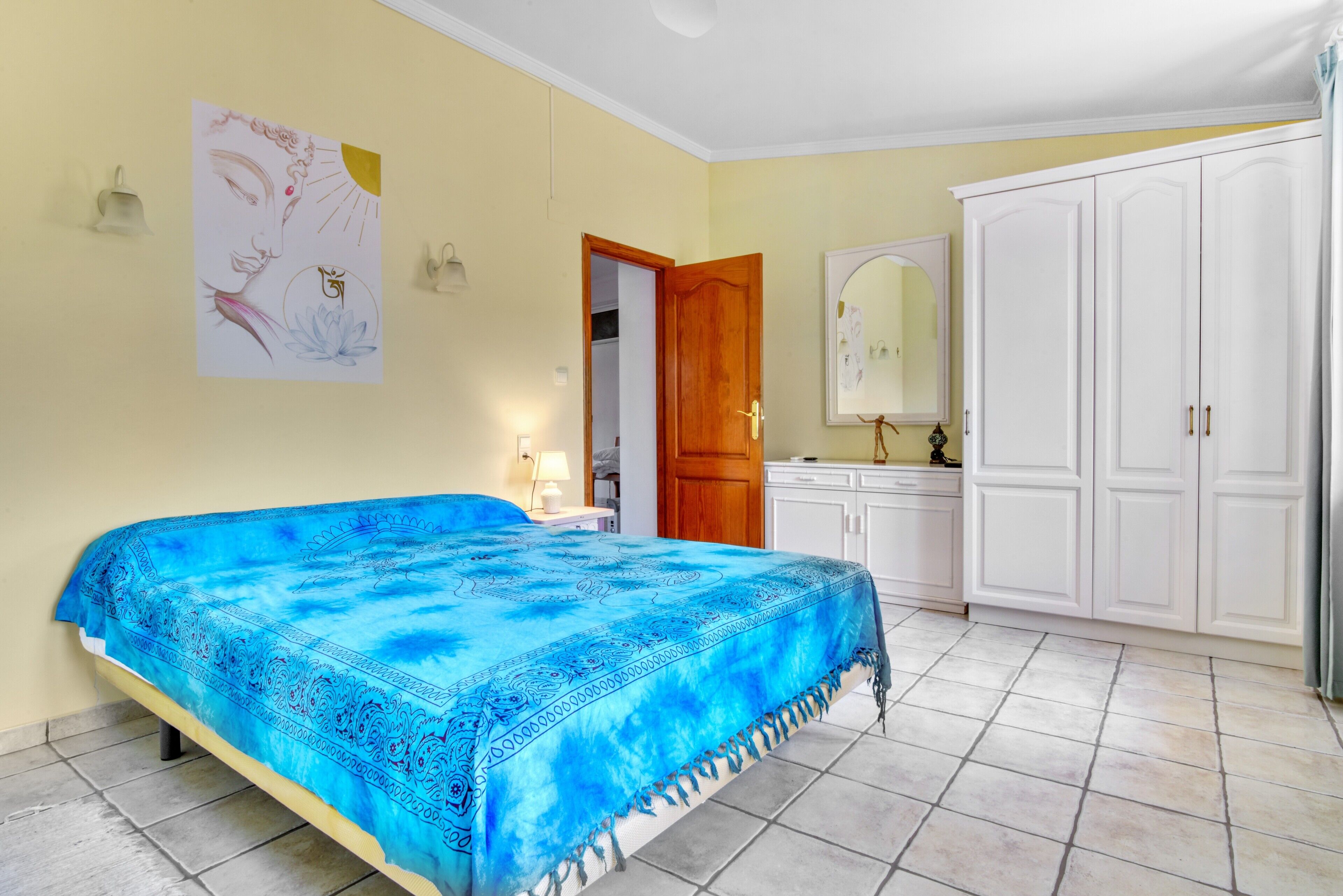 A bedroom with a bed, wardrobe, and a wall with artwork.