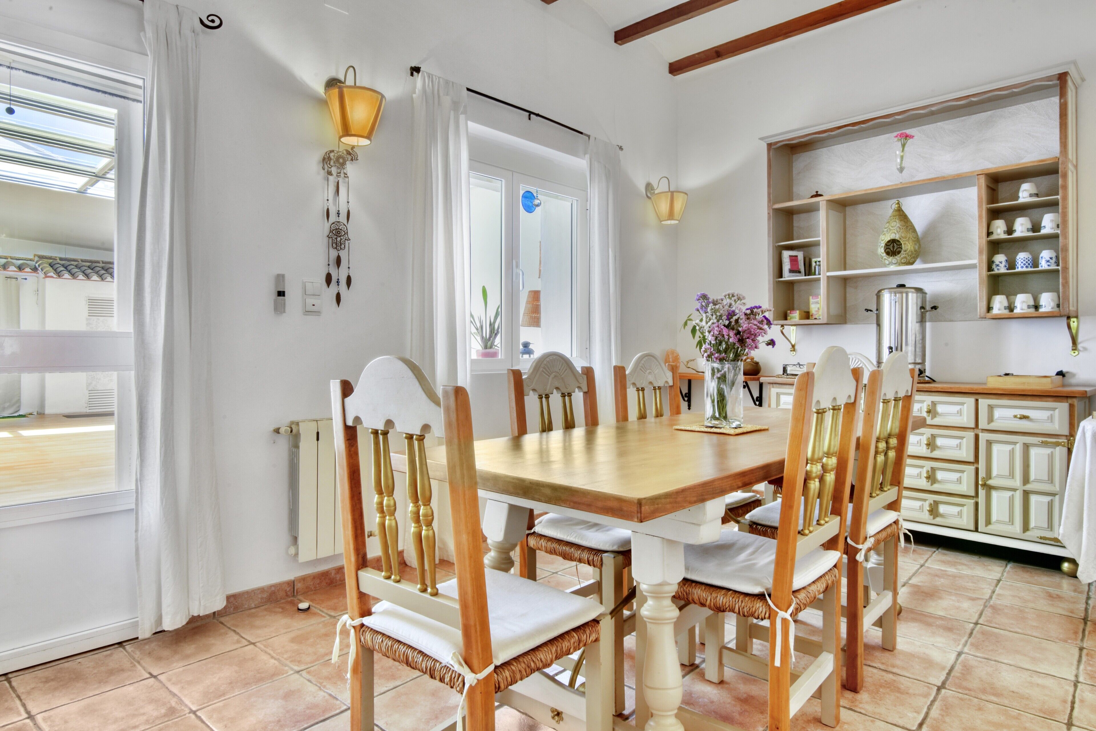 A dining area with a wooden table and chairs, a kitchen with cabinets, and a window with curtains.