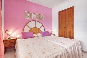 A bedroom with a bed, two nightstands, a wooden wardrobe, and three framed pictures on the wall.