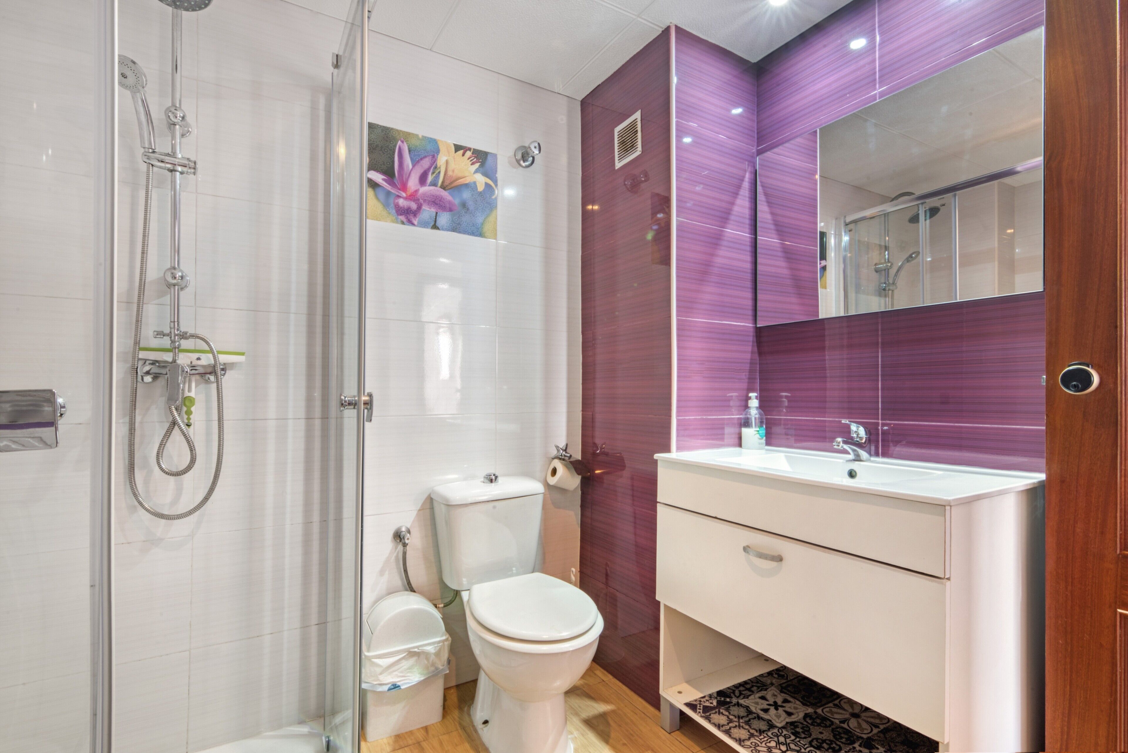 Un baño con cabina de ducha de vidrio, inodoro, lavabo con espejo y tocador de madera.