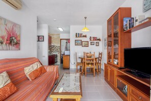 A living room with a sofa, a coffee table, a dining area with chairs, a television, and a bookshelf.