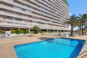 A hotel with a swimming pool, multiple balconies, and palm trees.