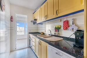 Una cocina con gabinetes amarillos, un lavabo doble, una cafetera y vistas a través de la puerta abierta.