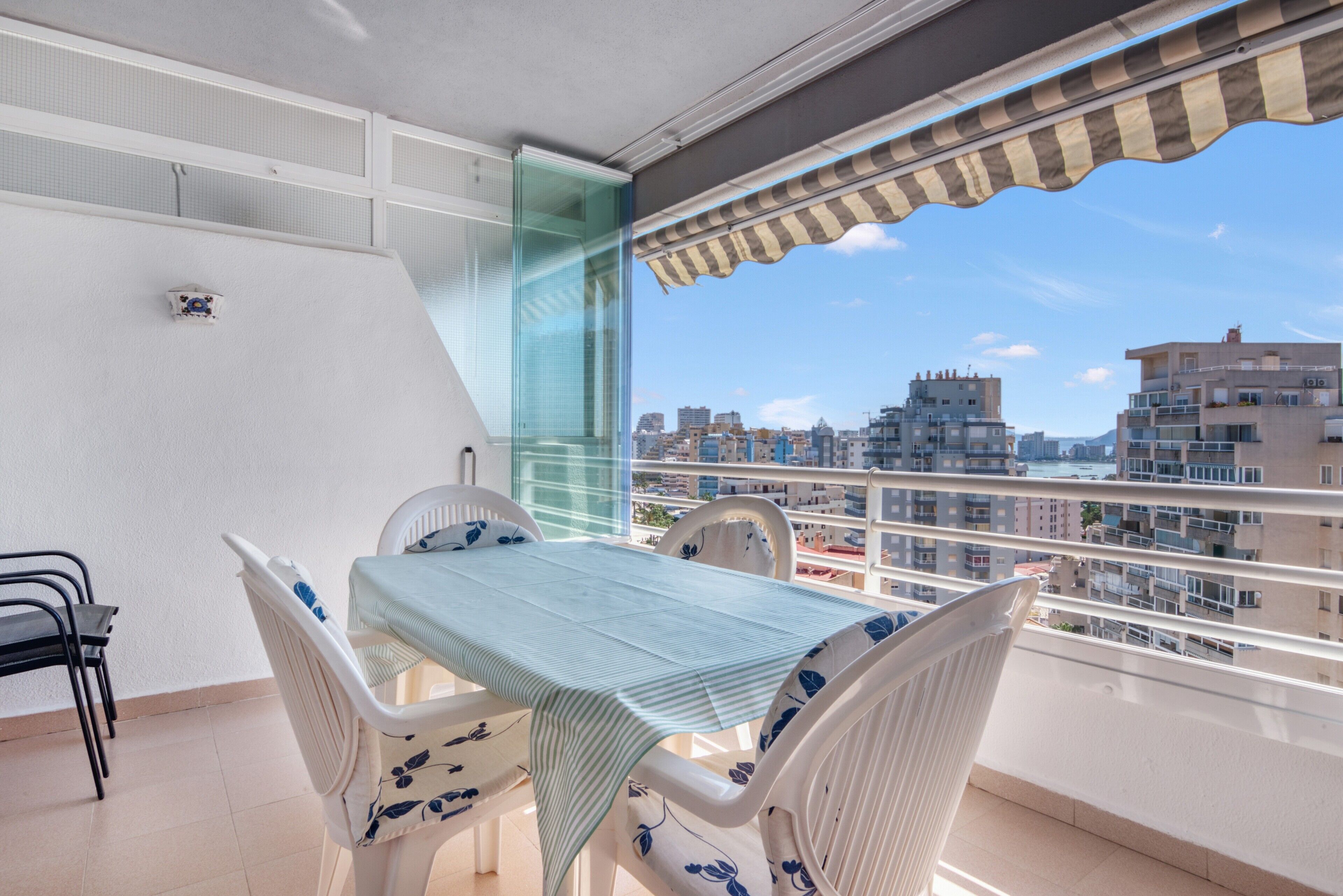 A balcony with a table and chairs, a glass partition, and a view of the cityscape.