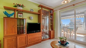 Een woonkamer met een televisie, houten kasten, een glazen kast en een balkon met stoelen.